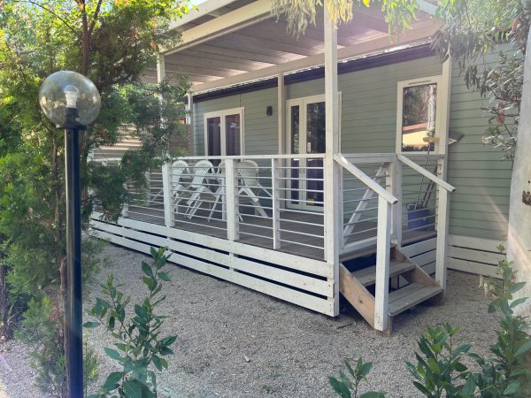 Una veranda in legno con sedie bianche e vegetazione intorno.