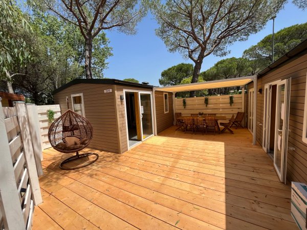Una terrazza in legno con poltrona sospesa e tavolo da pranzo sotto il pergolato.