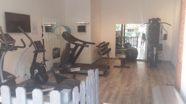 Una palestra con tapis roulant, cyclette e attrezzi vari, pavimento in legno chiaro.