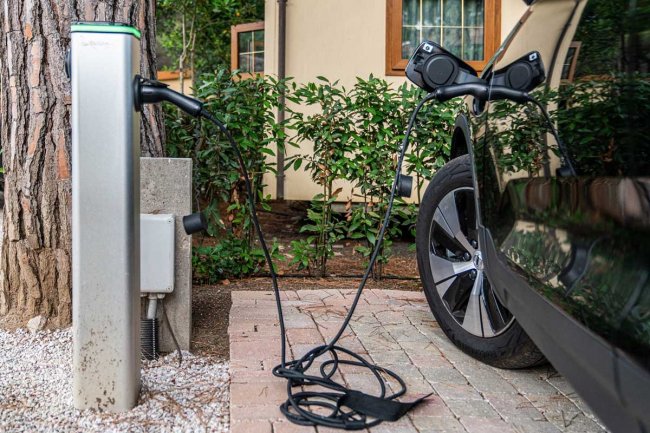 Auto elettrica in carica presso una stazione di ricarica, con verde sullo sfondo.