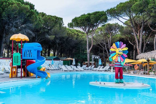 Una piscina con scivolo blu e rosso, e una statua colorata al centro. Alberi sullo sfondo.