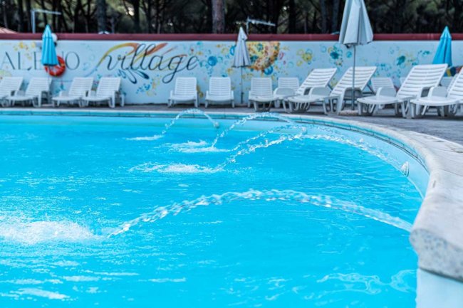 Piscina con sedie a sdraio e parete decorata.