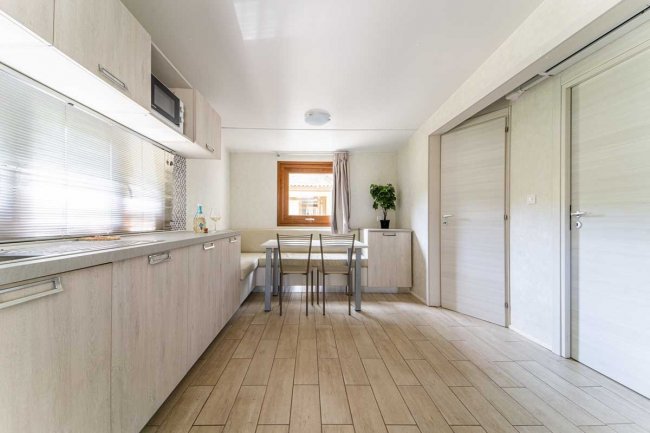 Cucina moderna con mobili in legno chiaro, tavolo con sedie e una finestra che illumina la stanza.