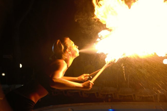 Una donna sputa fuoco da due torce accese in un ambiente oscuro.