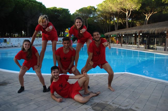 Sei persone in abiti rossi posano in un gruppo gioioso vicino a una piscina.