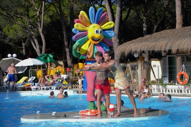 Persone in piscina accanto a una colorata statua di fiore sorridente.