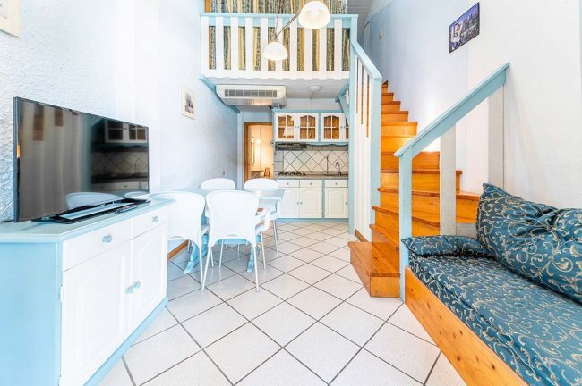 Interno moderno con soggiorno, cucina e soppalco. Arredamento bianco e azzurro.