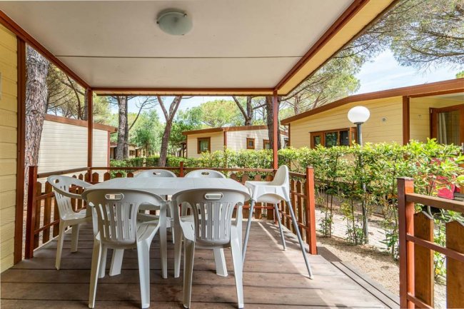 Veranda con tavolo e sedie bianche, circondata da bungalow e natura.