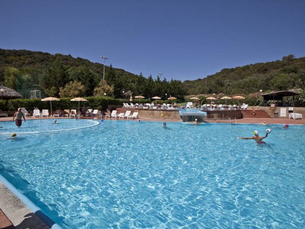 Piscina all'aperto con bagnanti e sedie a sdraio, circondata da colline.
