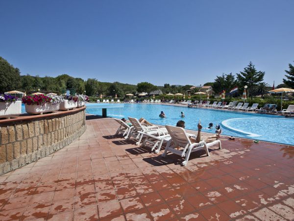 Piscina con nuotatori e sedie a sdraio bianche su un bordo bagnato, vista panoramica.