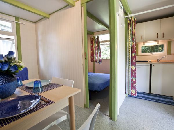 Interno di casa mobile con tavolo da pranzo, cucina compatta e camera da letto.