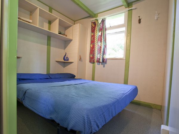 Una piccola stanza con un letto matrimoniale e scaffali, decorata con toni verdi e blu.