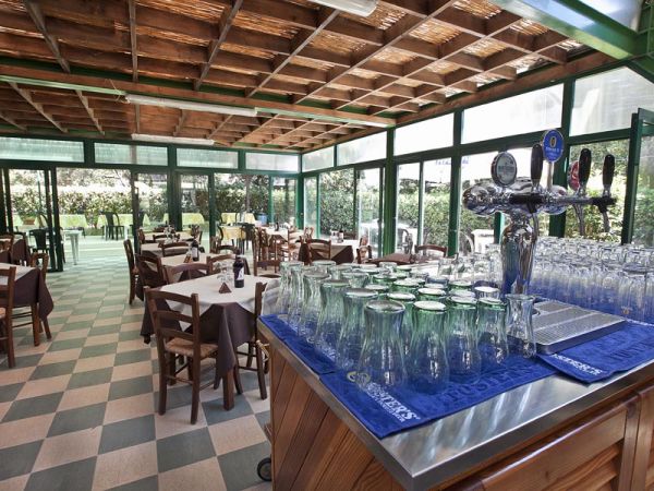 Interno di un ristorante con tavoli apparecchiati e un bancone con bicchieri.