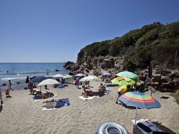 Spiaggia con ombrelloni colorati, persone che prendono il sole e mare sullo sfondo.