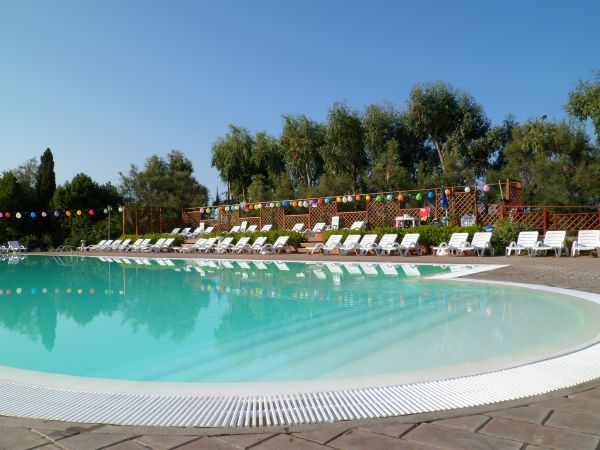 Piscina circondata da lettini bianchi e decorazioni colorate, alberi sullo sfondo.