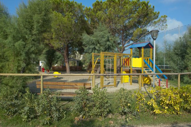 Parco giochi con strutture colorate circondato da alberi e cespugli.