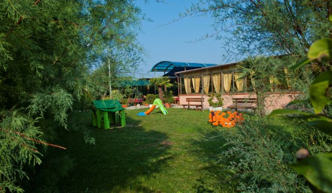 Spazio verde con giochi per bambini e una struttura con tende gialle.
