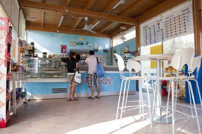 Due persone al bancone di una gelateria con interni azzurri e sedie bianche.