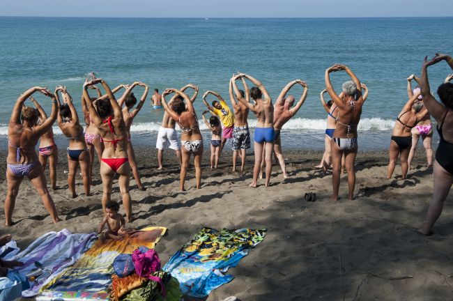 Gruppo di persone in costume da bagno fa stretching su una spiaggia.