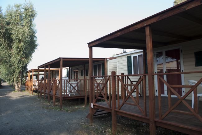 File di bungalow in legno con terrazze coperte, al bordo di un sentiero sterrato.