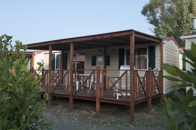 Una casa mobile in legno con veranda e sedie bianche.