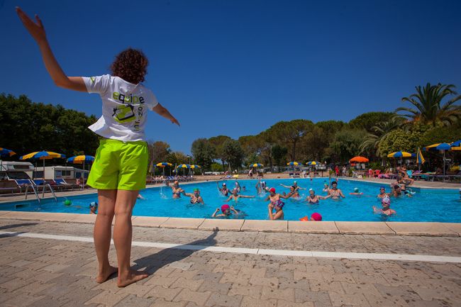 Persona guida un gruppo in piscina sotto un cielo blu.