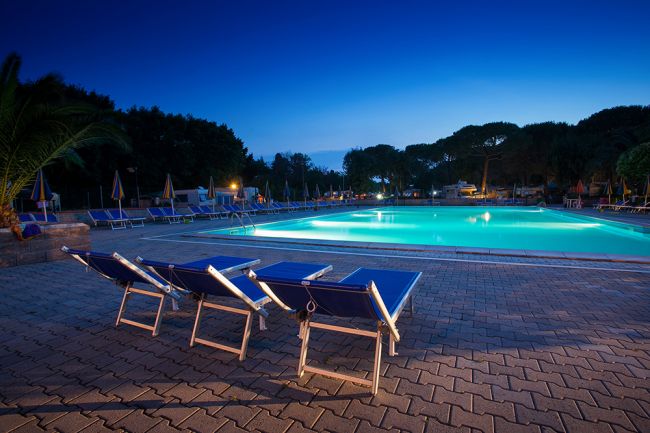 Piscina illuminata con lettini vuoti al tramonto.