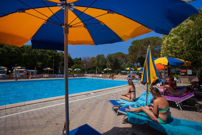 Persone rilassate su sdraio accanto a una piscina con ombrelloni colorati.