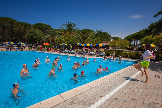 Lezione di acquagym in piscina con istruttore sulla riva.