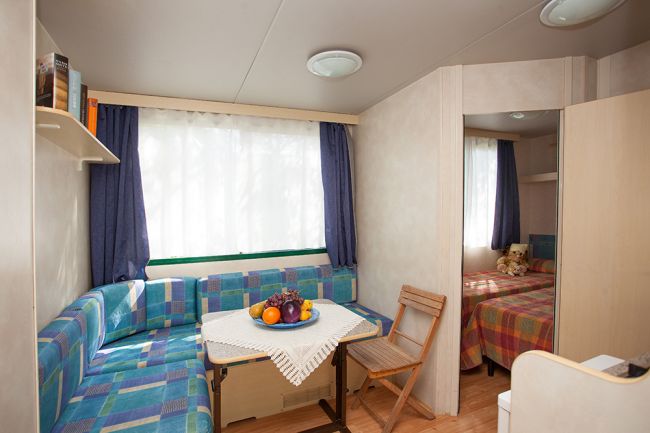 Soggiorno accogliente con divano a quadri e tavolo, vista su una camera da letto.