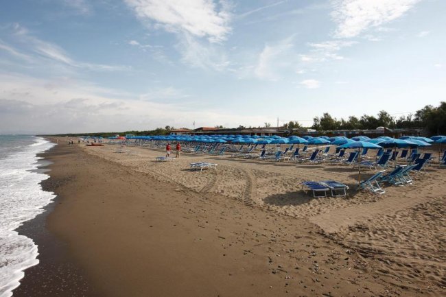 Spiaggia sabbiosa con file di sdraio e ombrelloni blu.