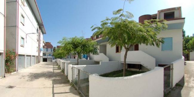 Vialetto con edifici moderni bianchi e alberi, piccole recinzioni attorno.