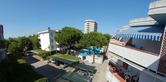 Complesso residenziale con balcoini e piscina, circondato da alberi.