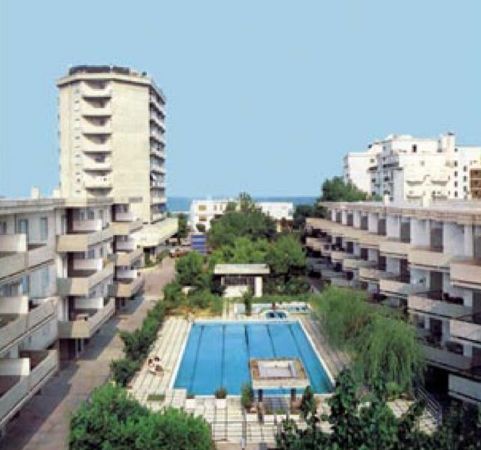 Complesso residenziale con piscina centrale, circondato da edifici e alberi sullo sfondo.