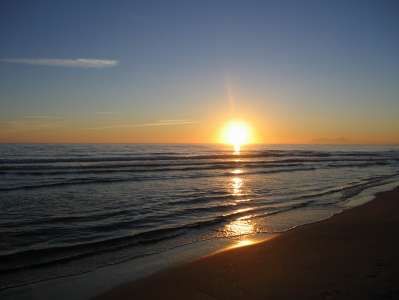 Tramonto sul mare con onde leggere e riflessi dorati in acqua.