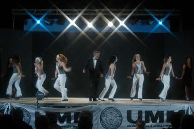 Performers in abiti eleganti e luci brillanti sul palco.