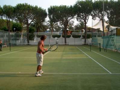 Una persona gioca a tennis su un campo all'aperto con alberi sullo sfondo.