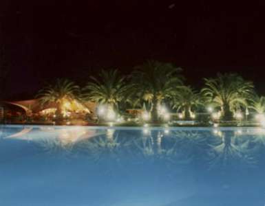 Piscina illuminata di notte, circondata da palme che si riflettono nell'acqua.
