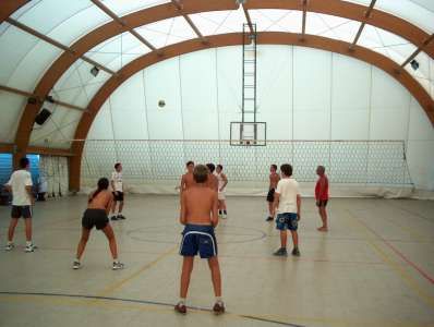 Persone giocano a pallavolo in una struttura coperta con tetto ad arco.