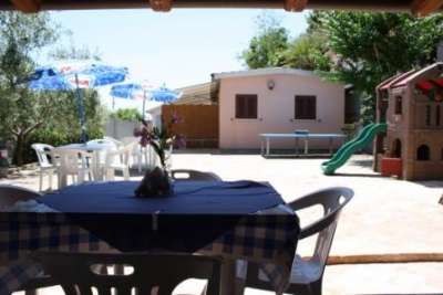 Tavolo coperto con tovaglia a quadretti, vista su cortile con casetta-gioco e scivolo.
