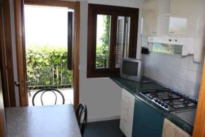 Cucina compatta con un piano cottura, tavolo e finestra che si apre su un balcone con piante verdi.