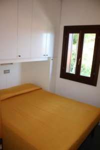 Camera da letto con copriletto arancione, finestra con vista verde.