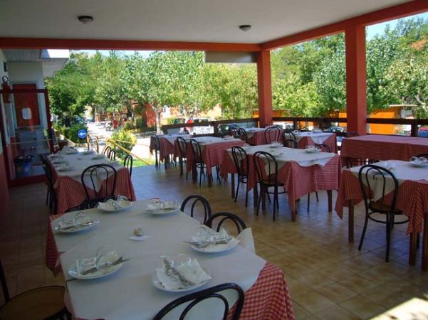 Una terrazza con tavoli apparecchiati, tovaglie a quadri rossi e bianchi, circondata dalla natura.