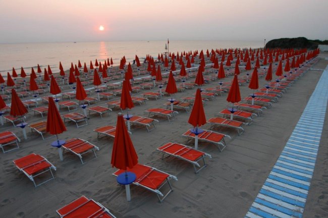 Spiaggia al tramonto con lettini e ombrelloni chiusi.