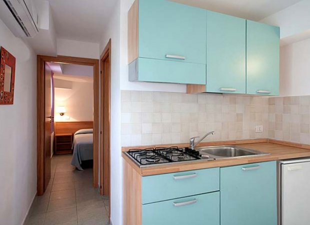 Cucina con mobili azzurri e camera sullo sfondo.