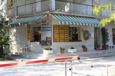Edificio con tende a righe e cartelli, circondato da piante in vaso.