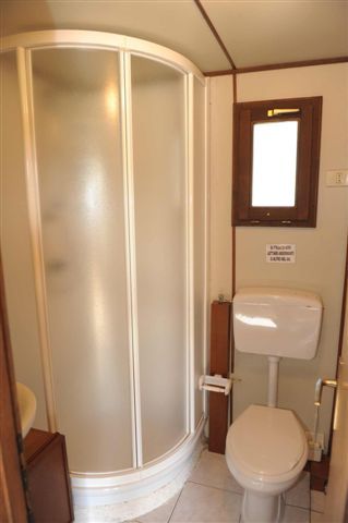 Un bagno con una doccia semicircolare e un gabinetto sotto una piccola finestra.