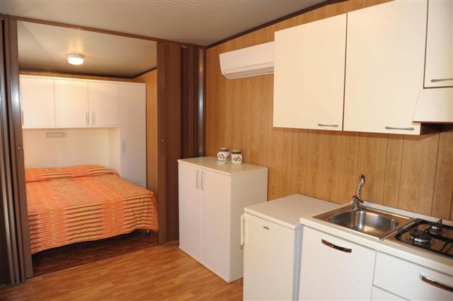 Un monolocale con cucina moderna, letto matrimoniale e pavimento in legno.