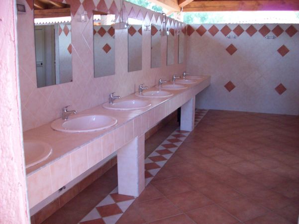 Una fila di lavandini con specchi sopra in un bagno piastrellato.