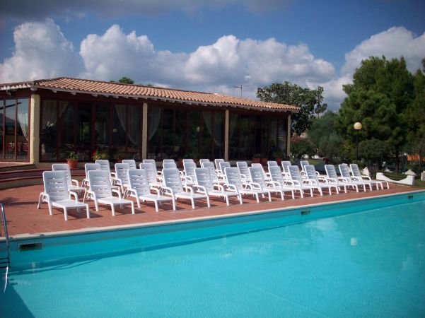 Piscina con sedie a sdraio bianche allineate e un edificio con tetto in tegole.